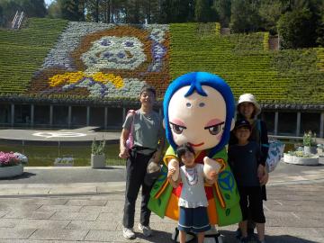 花と緑のタペストリーの前で家族連れの来園者と記念写真